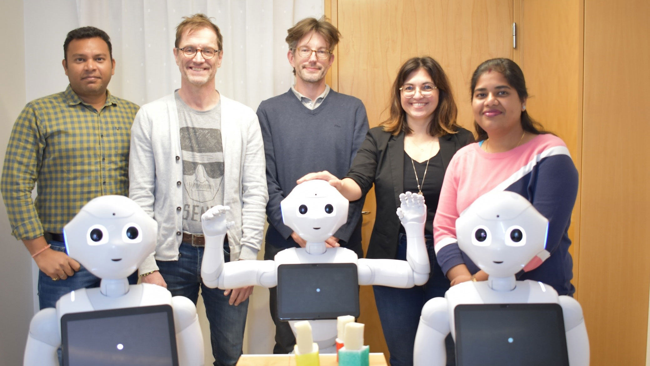 Forskargrupp vid Umeå universitet tilslammans med tre robotar Pepper.